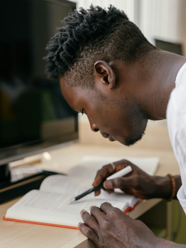 Jovem negro estudando concentrado com livro e caneta — liderança emergente em formação